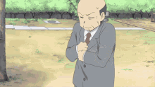 a bald man in a suit and tie stands in a park