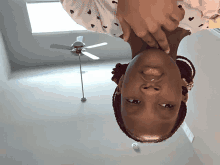 a girl is upside down in a room with a ceiling fan in the background