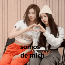 two girls are sitting next to each other making a heart shape with their hands and the words somos de mich above them