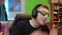 a man wearing sunglasses and headphones is sitting in front of a green wall