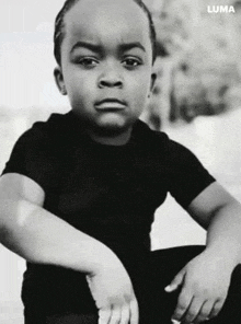 a black and white photo of a young boy wearing a black shirt and sitting down .