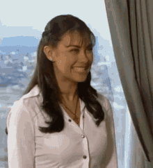 a woman in a white shirt is standing in front of a window smiling .