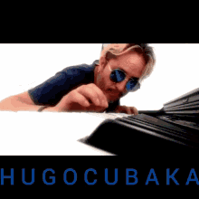 a man wearing sunglasses is playing a piano and the name hugocubaka is on the bottom of the image