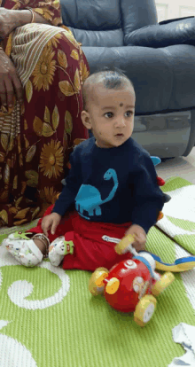 a baby wearing a shirt with a dinosaur on it sits on the floor