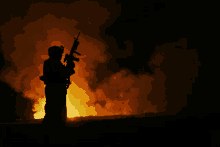 a man holding a gun in front of a large fire