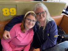 two women are posing for a picture in front of a sign with the number 89 on it