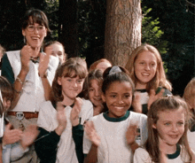 a group of girl scouts are clapping in front of a tree and their uniforms say girl scouts on them