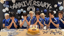 a group of young men praying in front of a cake that says 3 year