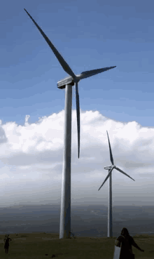 two wind turbines on a hill with a blue sky and clouds