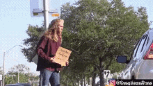 a man with long hair is walking down the street holding a sign that says i love you to the moon and back .