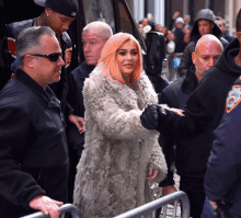 a woman with pink hair and a fur coat is surrounded by a group of men