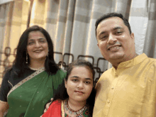 a man in a yellow shirt stands next to a woman in a green sari and a girl in a red dress