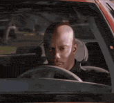 a man with a bald head is driving a car and looking at the camera