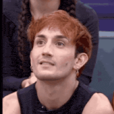 a man with red hair and earrings is wearing a black tank top and looking up .
