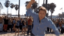 a man in a blue shirt is dancing in front of a crowd on the beach