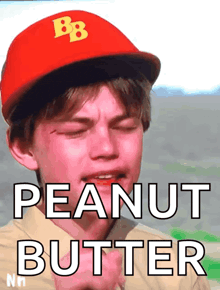 a boy wearing a red hat with the letter b on it is eating peanut butter