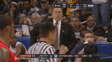 a man in a suit and tie stands in front of a crowd watching a basketball game between cincinnati and louisville