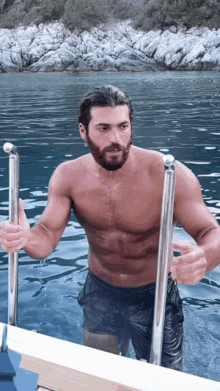 a shirtless man with a beard is holding onto a metal railing in the water