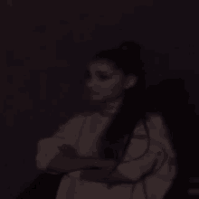 a woman in a white shirt is sitting in a dark room with her arms crossed .