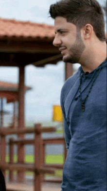 a man in a blue shirt with a necklace around his neck stands in front of a gazebo