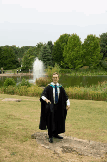 a man in a graduation gown stands in front of a pond