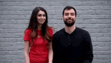 a man and a woman are standing next to each other and smiling in front of a brick wall .