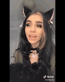 a woman wearing cat ears and a cat collar has a tiktok sticker on her face