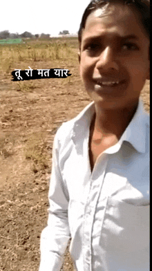 a young man in a white shirt stands in a field with a sign that says ' tul so mat yaar '