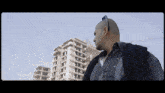 a bald man wearing sunglasses stands in front of a tall building under construction