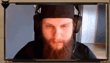 a man with a beard wearing headphones and a hat is looking at the camera .