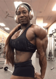 a very muscular woman wearing headphones holds a barbell in a gym