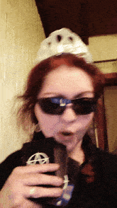 a woman wearing sunglasses and a paper hat holds a cup
