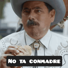 a man in a cowboy hat is eating a chicken sandwich with the words no ta conmadre below him