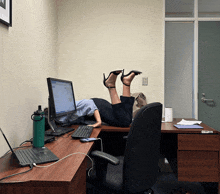 a woman is laying on a desk with her feet up in front of a computer