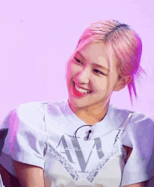 a woman with pink hair is smiling and wearing a white t-shirt with the letter a on it .