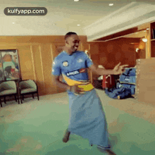 a man in a blue shirt and a blue skirt is dancing in a living room .