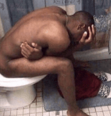 a naked man is sitting on a toilet holding his head