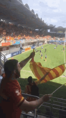 a man in a red shirt holds a yellow and orange flag in front of a stadium that has oneet written on it