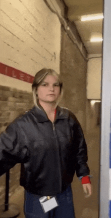 a woman wearing a black leather jacket is standing in a hallway .