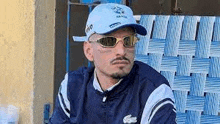 a man wearing a blue hat and sunglasses is sitting on a chair .