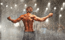 a shirtless boxer is standing in the rain with his arms outstretched