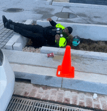 a man is laying on the ground next to an orange cone and a cup of coffee