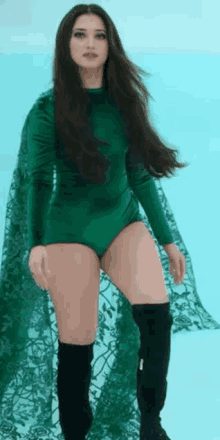 a woman is wearing a green bodysuit and black boots .