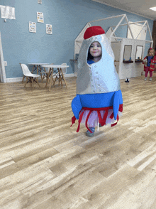 a little girl wearing a rocket costume is walking on a wooden floor