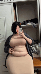 a woman is taking a selfie in front of a mirror with her phone .