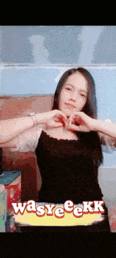 a woman making a heart shape with her hands in front of a sign that says wasyeeekk