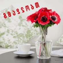 a vase of red flowers sits on a table with a cup of coffee