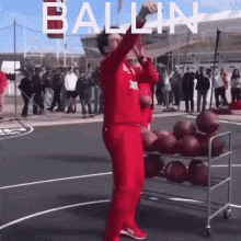 a man in a red suit is standing in front of a cart of basketballs with the word ballin written on it