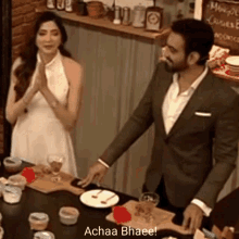 a man in a suit and a woman in a white dress are standing at a table with food .