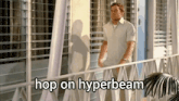 a man is standing on a balcony with the words hop on hyperbeam above him